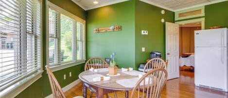 A dining area with a round wooden table and six wooden chairs, a green wall, and a white ceiling.