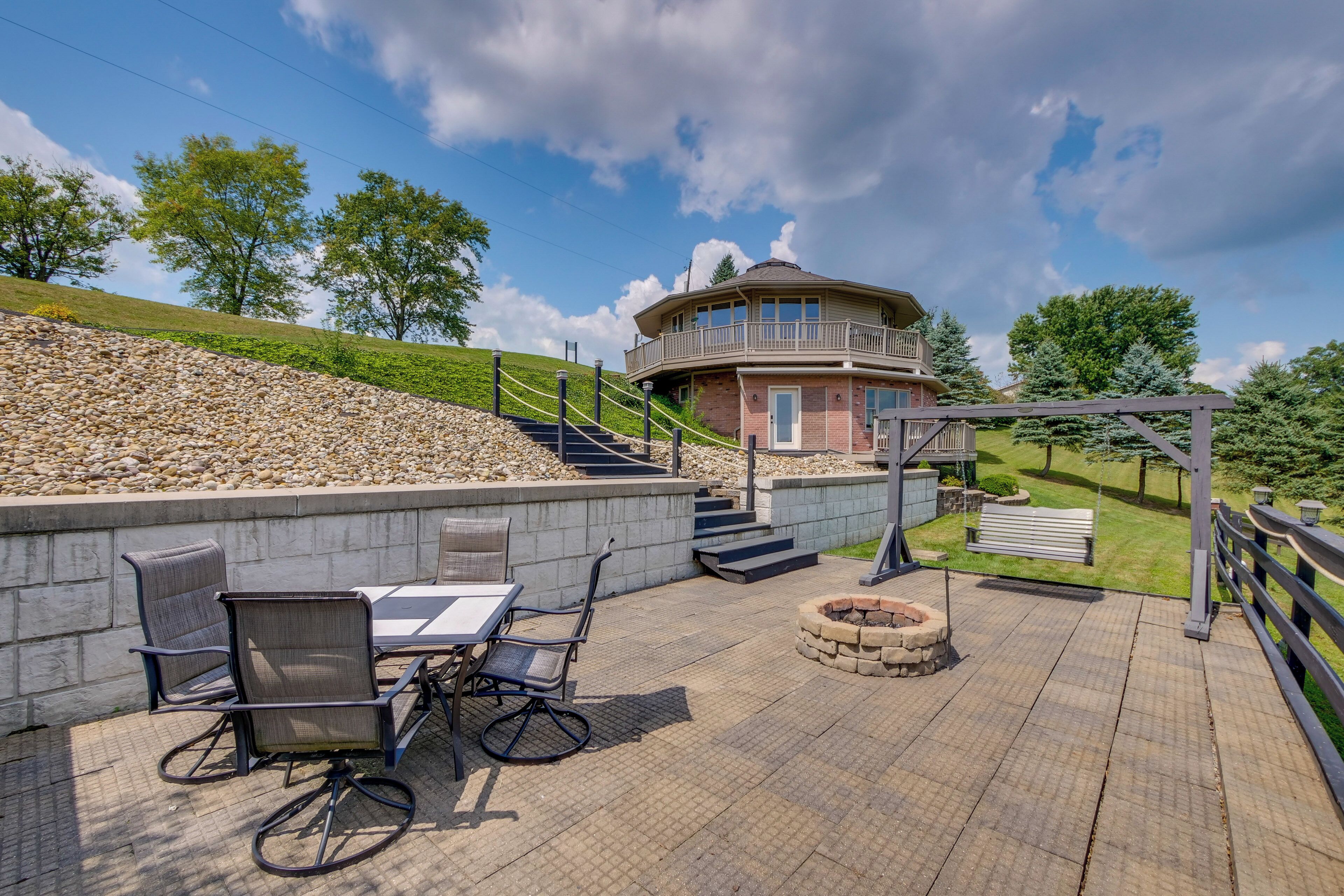 A circular building with a balcony, a stone retaining wall, outdoor seating, and a fire pit.