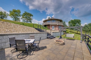 Een rond gebouw met een balkon, een stenen steunmuur, terrasmeubilair en een vuurkorf.