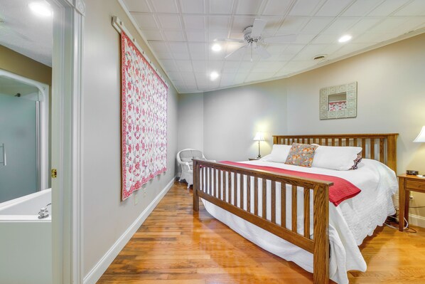 Un dormitorio con una cama de madera, una mesita de noche, una lámpara, un ventilador de techo y un baño con bañera.