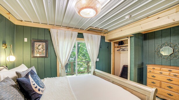 A bedroom with a large bed, wooden dresser, and a view of greenery outside. - Private Island: Home in Belding w/ Dock & Grill! (Belding)