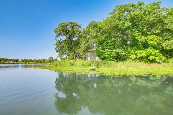 A serene lakeside property with a house surrounded by lush greenery and trees. - Private Island: Home in Belding w/ Dock & Grill! (Belding)