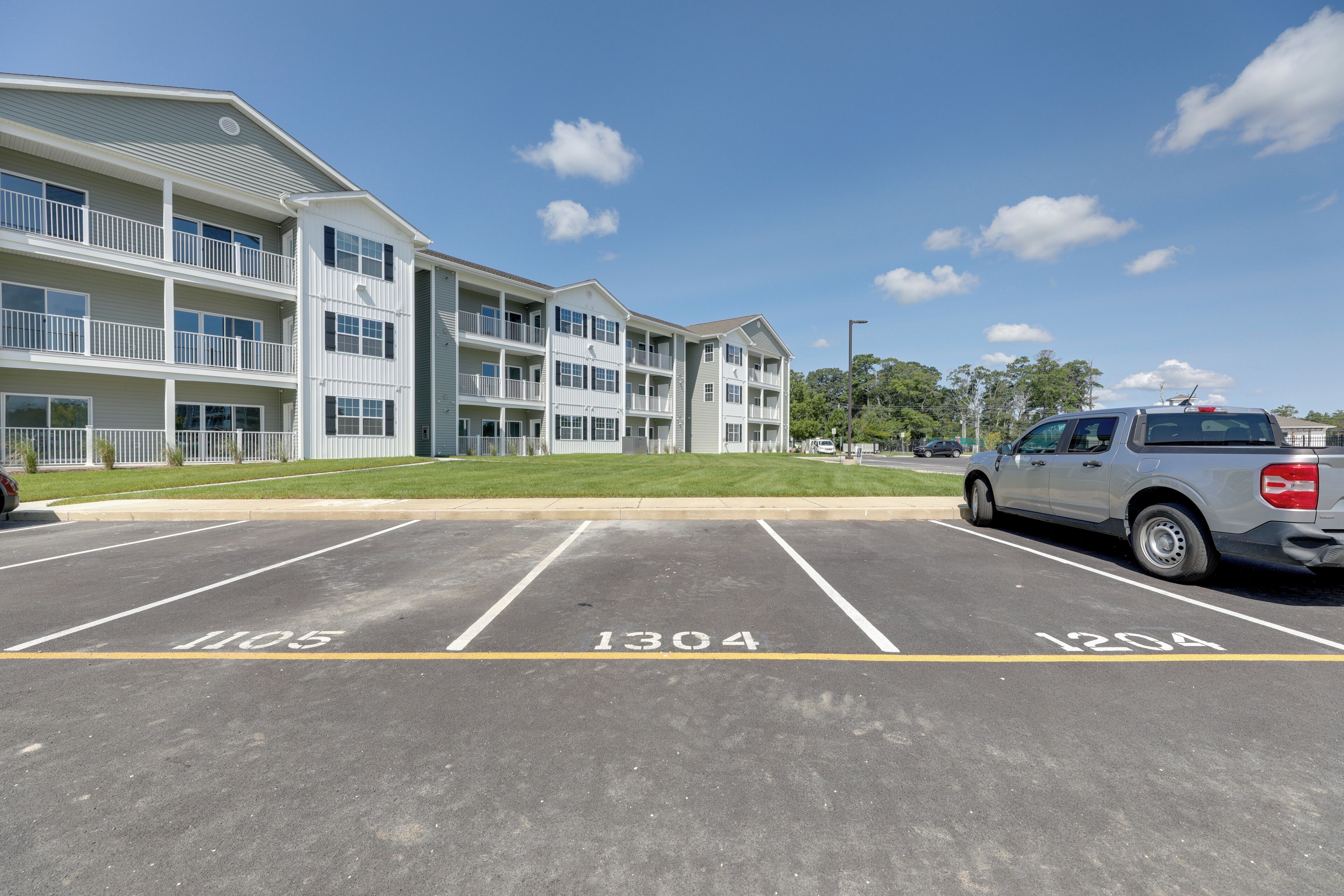 Un parking avec des emplacements numérotés (1105, 1304 et 1204), situé à côté d’un immeuble à plusieurs étages doté de balcons.