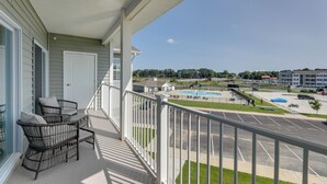 A balcony with wicker furniture, a view of a parking lot, and buildings in the background. - Bayfront Condo w/ Pool Access, Near Rehoboth Beach (Lewes)