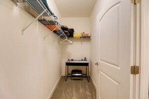 A narrow hallway with a door on the right, a small desk with a basket, and a metal shelf with hanging items. - Bayfront Condo w/ Pool Access, Near Rehoboth Beach (Lewes)