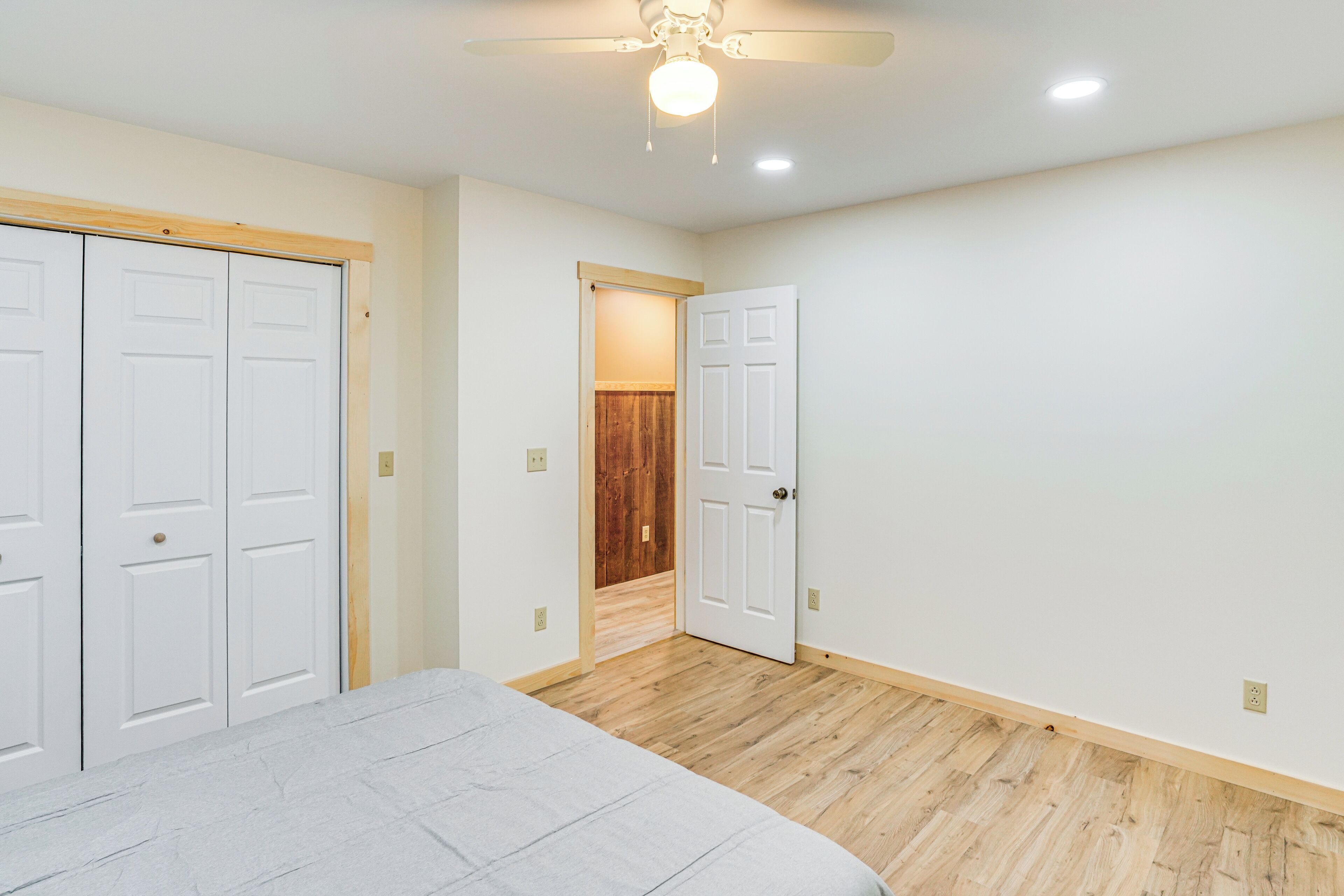 A bedroom with a bed, a ceiling fan, and wooden flooring.