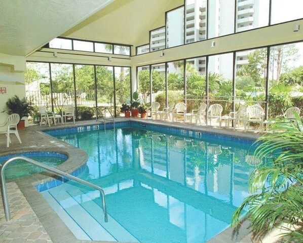 An indoor swimming pool with clear glass walls, surrounded by white chairs and potted plants. - 6165 Carrier Drive #1001 (Orlando)