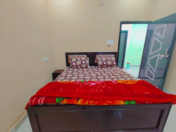 A bedroom with a bed, two nightstands, a red blanket, and a door with geometric patterns. - Saryu Lodge (Faizabad)