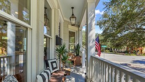 A covered porch with a bench, potted plants, and an American flag. - Luxurious, Bright, Chic Home on Treelined Street by Lucky Savannah (Savannah)