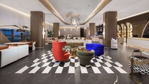 Un moderno vestíbulo de hotel con piso a cuadros, mobiliario contemporáneo y un candelabro central.