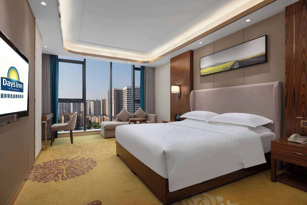 Una habitación de hotel con una cama grande, un escritorio, una silla, un sofá y un ventanal con vistas a la ciudad.