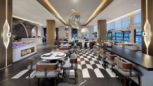 Un hall d’hôtel moderne avec un sol à carreaux, un bar, des espaces salon et un luminaire décoratif central.
