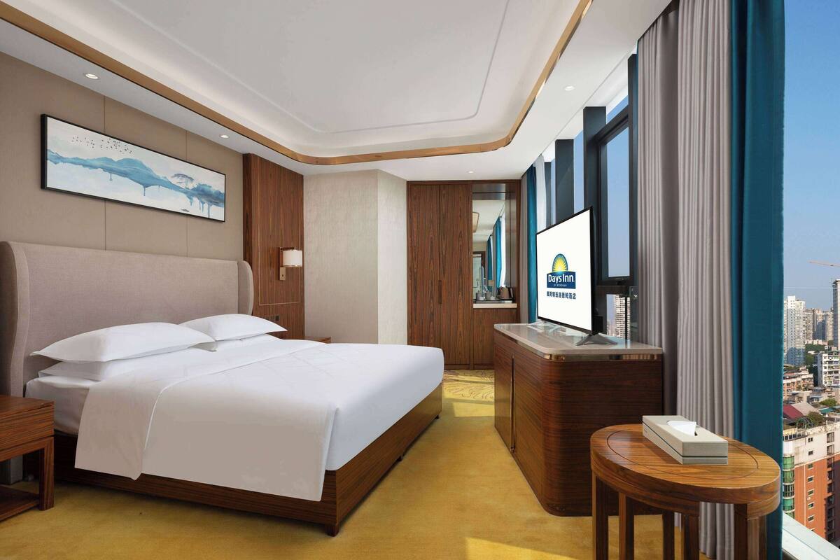 Habitación de hotel con cama, escritorio, televisor y vista a la ciudad.
