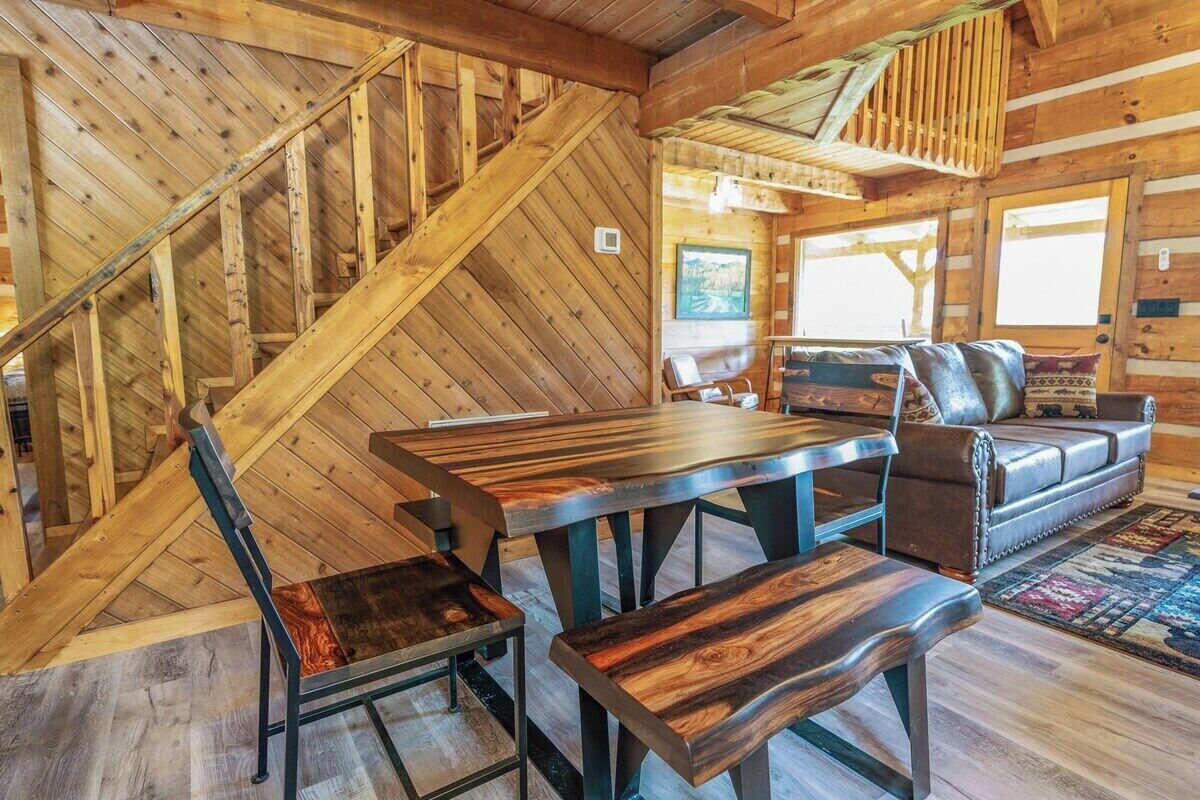 A rustic wooden interior with a dining table, chairs, a sofa, and a staircase.