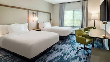 A hotel room with two beds, a desk with a chair, a TV, and a window with curtains.