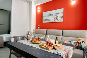 Un coin repas avec une table dressée pour deux personnes, un canapé et un tableau accroché au mur.