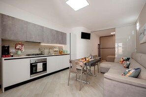 A modern kitchen with a dining area, a sofa, and a flat-screen TV.