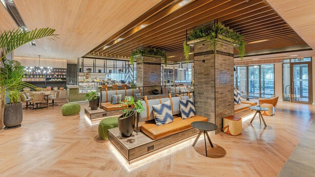 A modern interior with wooden flooring, seating areas, and large windows.