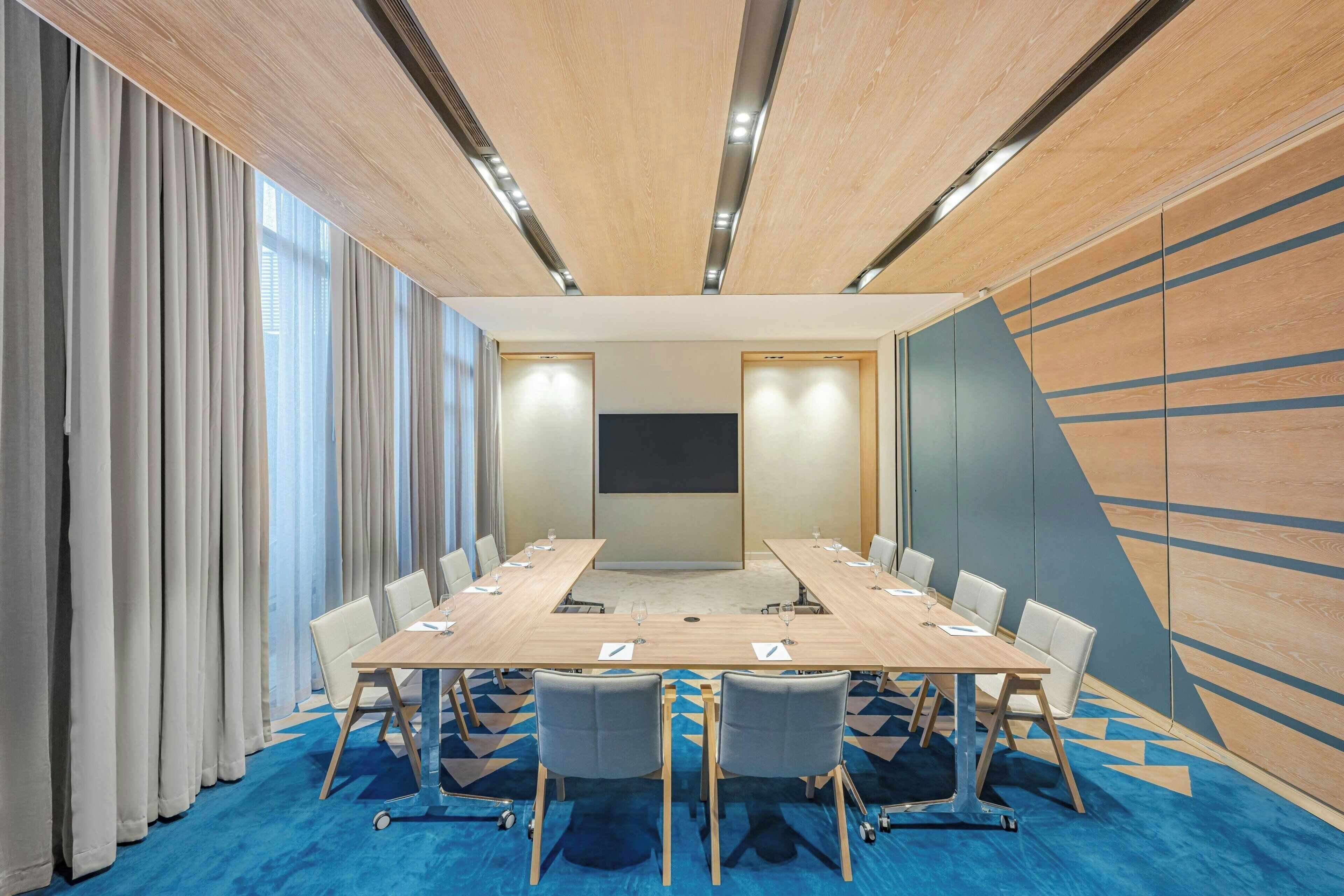 A conference room with a large table, chairs, a projector screen, and a blue carpet.
