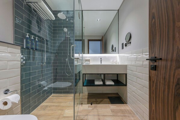 A modern bathroom with a glass-enclosed shower, a white sink with a mirror, and a wooden door. - Four Points BY Sheraton King Abdulaziz (Riyadh)