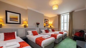 A hotel room with three beds, each with white linens and red accents, a green carpet, and a large window with curtains.