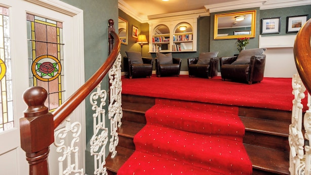 A staircase with red carpet leading to a seating area with leather chairs and a bookshelf.