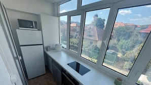 Cocina compacta con refrigerador, microondas y estufa, ventanas amplias con vistas a una iglesia y edificios residenciales.