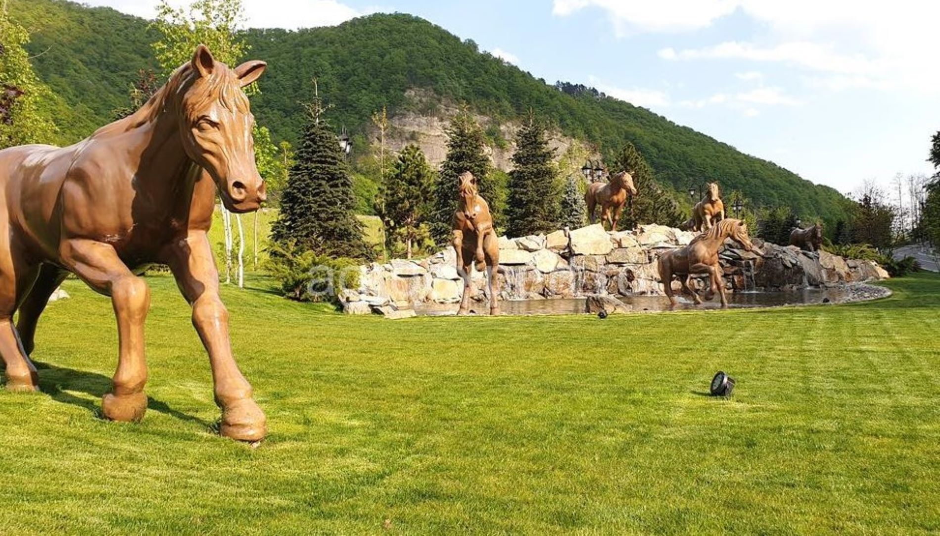 Une grande statue de cheval se dresse dans un espace verdoyant, avec une chaîne de montagnes en arrière-plan.