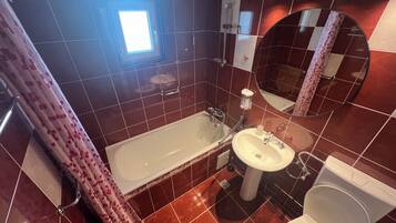 Et badeværelse med badekar, vask, toilet og et spejl.