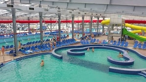 Una piscina techada con múltiples carriles, un tobogán acuático y sillas de descanso.