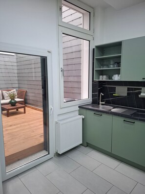 A modern kitchen with green cabinets, a black countertop, and a sliding glass door leading to a patio area with a wooden table and chairs.