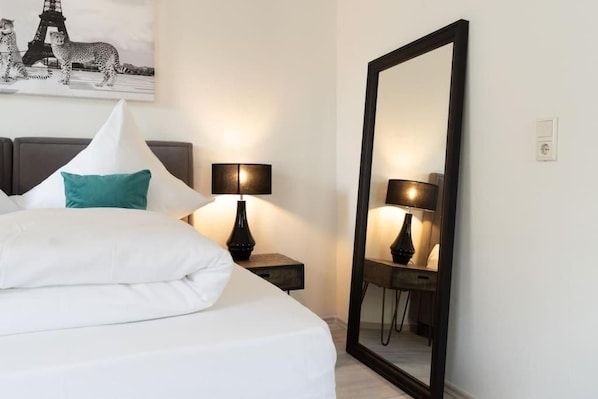A hotel room with a bed, two bedside lamps, a large mirror, and a painting of cheetahs on the wall.
