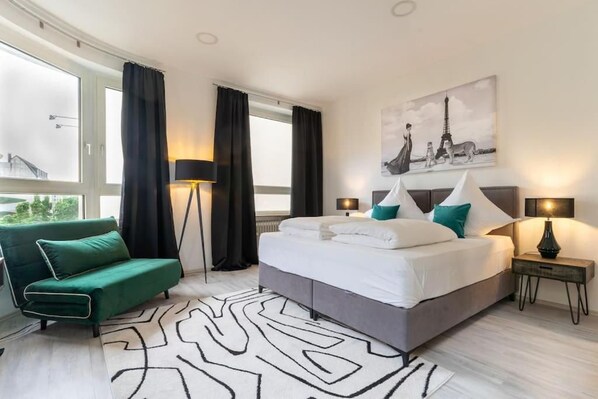 A modern bedroom with a bed, a green sofa, a floor lamp, and a painting of the Eiffel Tower.