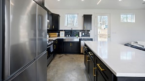 Una cocina moderna con electrodomésticos de acero inoxidable, armarios negros y encimera blanca.