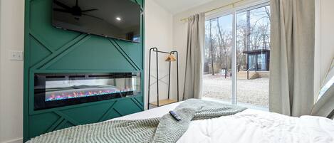 Un dormitorio moderno con una televisión instalada en una pared verde, una chimenea y un ventanal con cortinas.