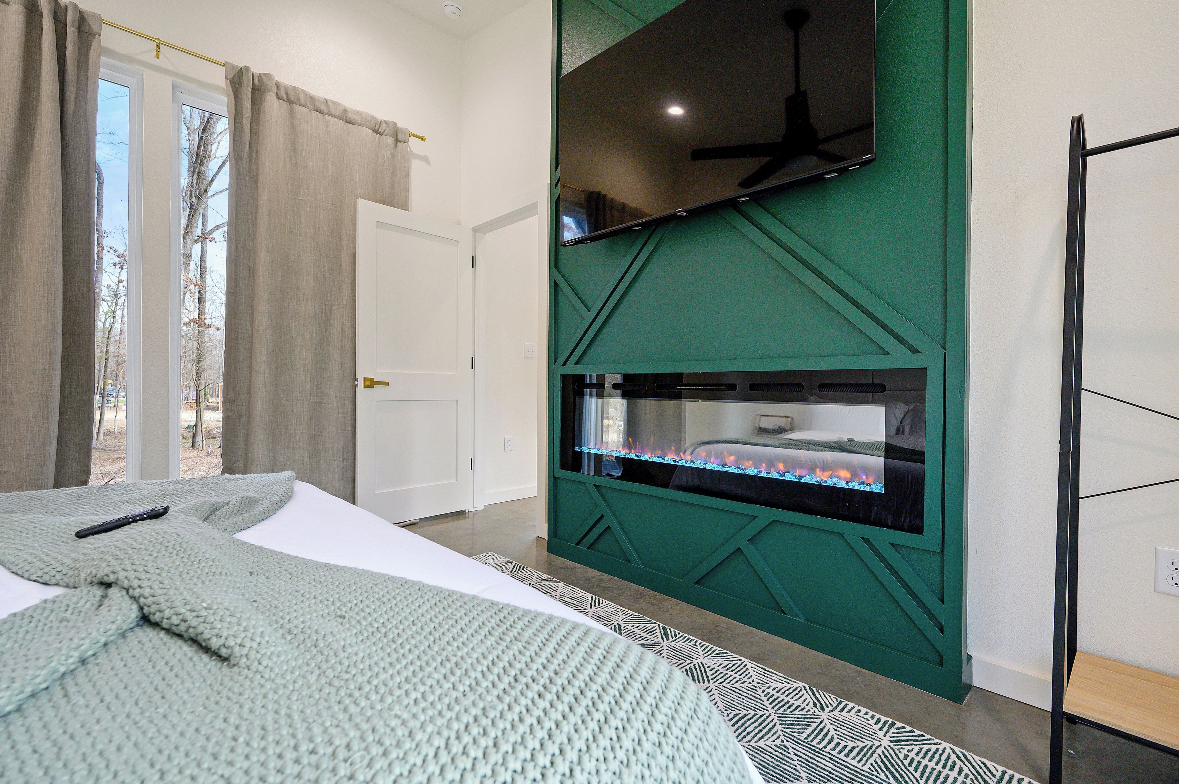 Een slaapkamer met een bed, een televisie aan een groene muur, en een raam met gordijnen.