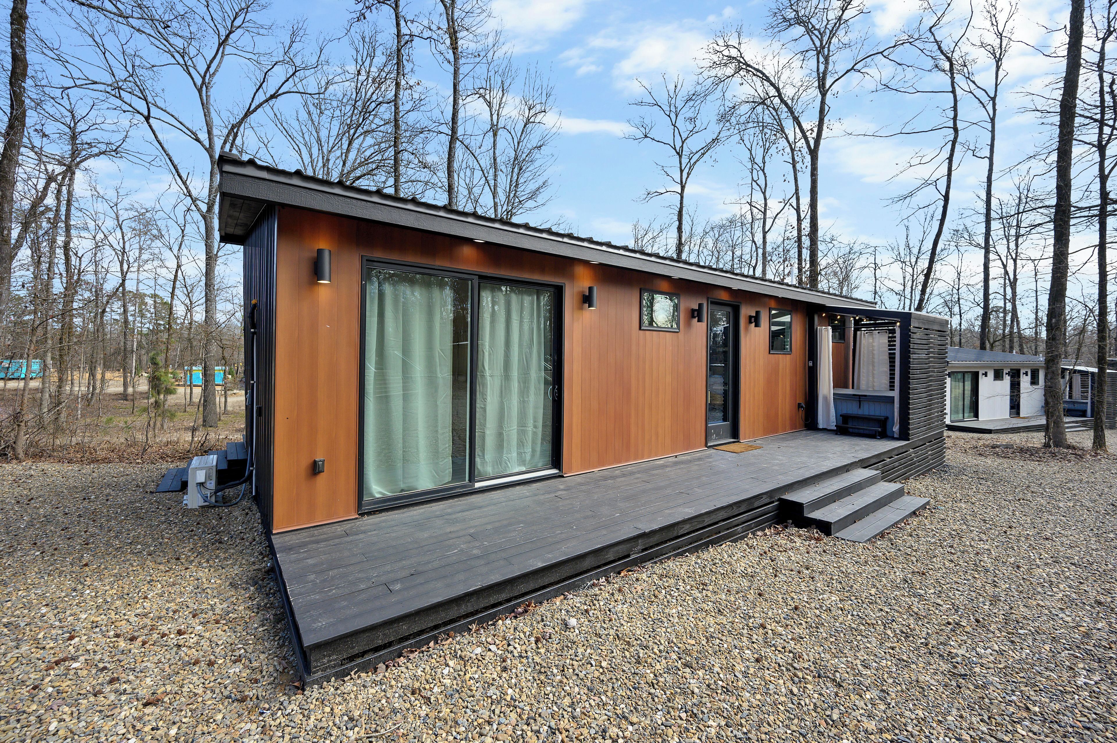 A modern, single-story cabin with a wooden exterior, large sliding glass doors, and a small porch area.