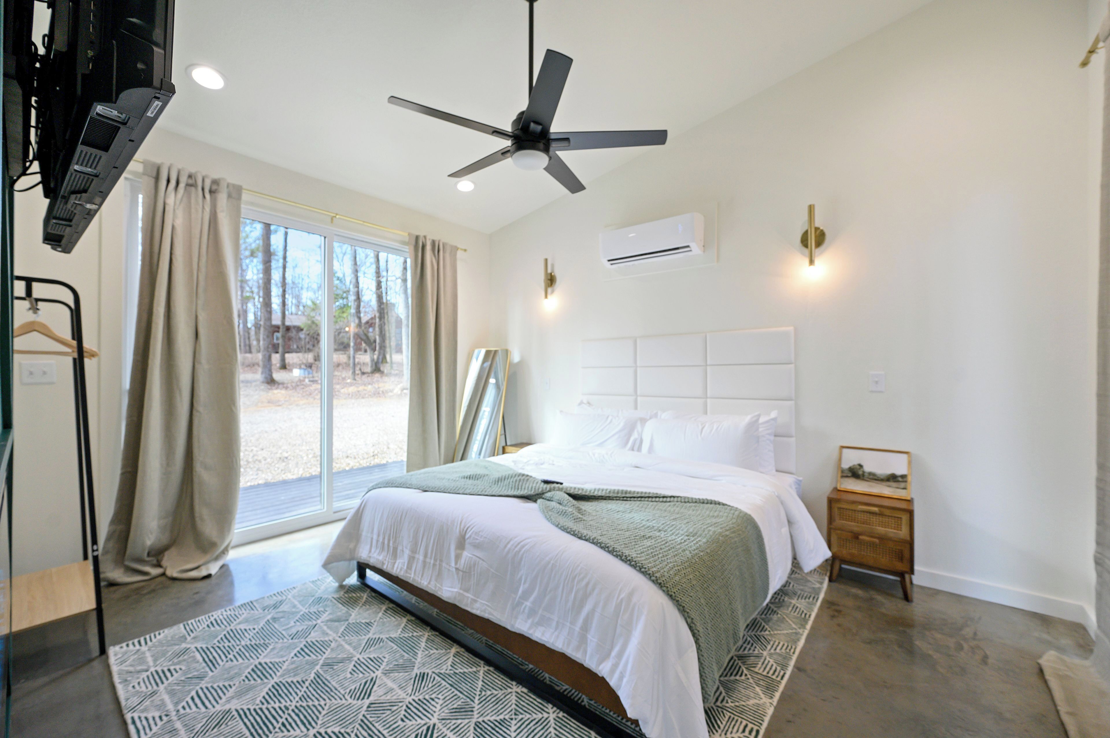 A modern bedroom with a large bed, a ceiling fan, a window with curtains, and a small bedside table with a lamp.
