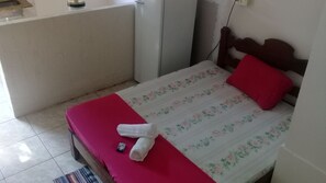 Un petit lit bien fait, avec une couverture à motifs floraux, un oreiller rouge et une serviette enroulée.