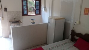 Une petite pièce, peu meublée, avec un lit, un petit lavabo et un réfrigérateur.