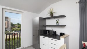 A modern kitchen with a built-in refrigerator, microwave, and coffee maker, a dining area with a chair, and a balcony with a view of buildings and greenery.