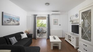 A living room with a sofa, a coffee table, a TV stand, and a painting of boats on the wall.