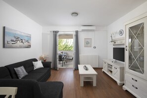 A living room with a sofa, a coffee table, a TV stand, and a painting of boats on the wall. - Apartments Heidi with shared Pool (Ap 2) (Nova Vas)