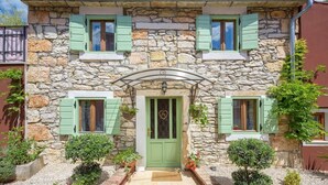 A stone building with a green door, two windows with shutters, and a small garden with potted plants. - Rustic Casa Dvi Mendule with swimming pool (Nova Vas)