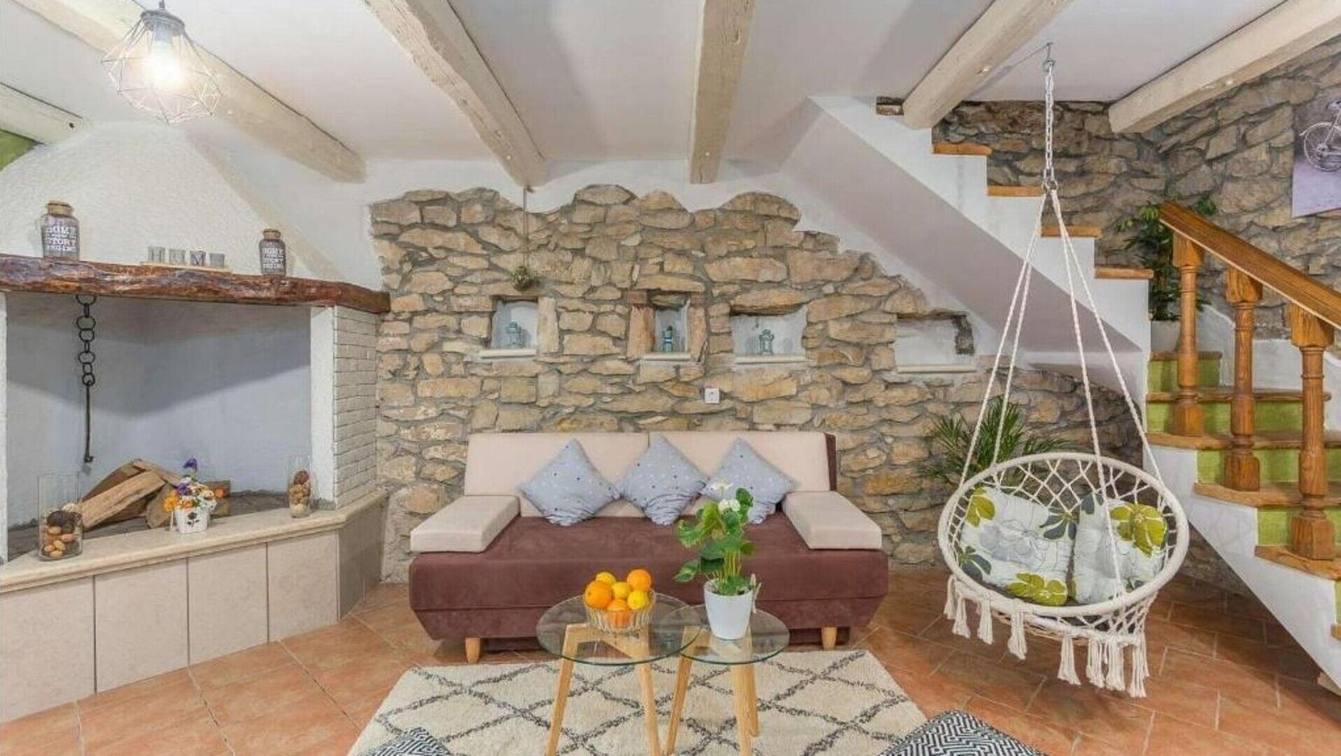 A cozy living room with a stone wall, a sofa, a hanging chair, and a staircase.