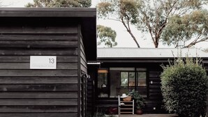 A wooden cabin with a number sign, a small porch, and a view of trees.