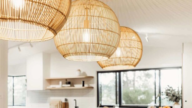 A modern kitchen with white cabinets, a wooden dining table, and three large woven pendant lights.