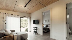 A modern living room with a grey sofa, a TV mounted on the wall, and a sliding door leading to a bedroom.