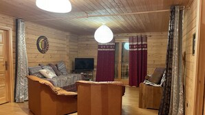 A cozy wooden cabin interior with a sofa, a TV, and a dining area. - Le Grand Chalet (Gérardmer)