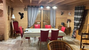 A wooden interior with a dining table, red chairs, a plaid curtain, and a ceiling lamp. - Le Grand Chalet (Gérardmer)